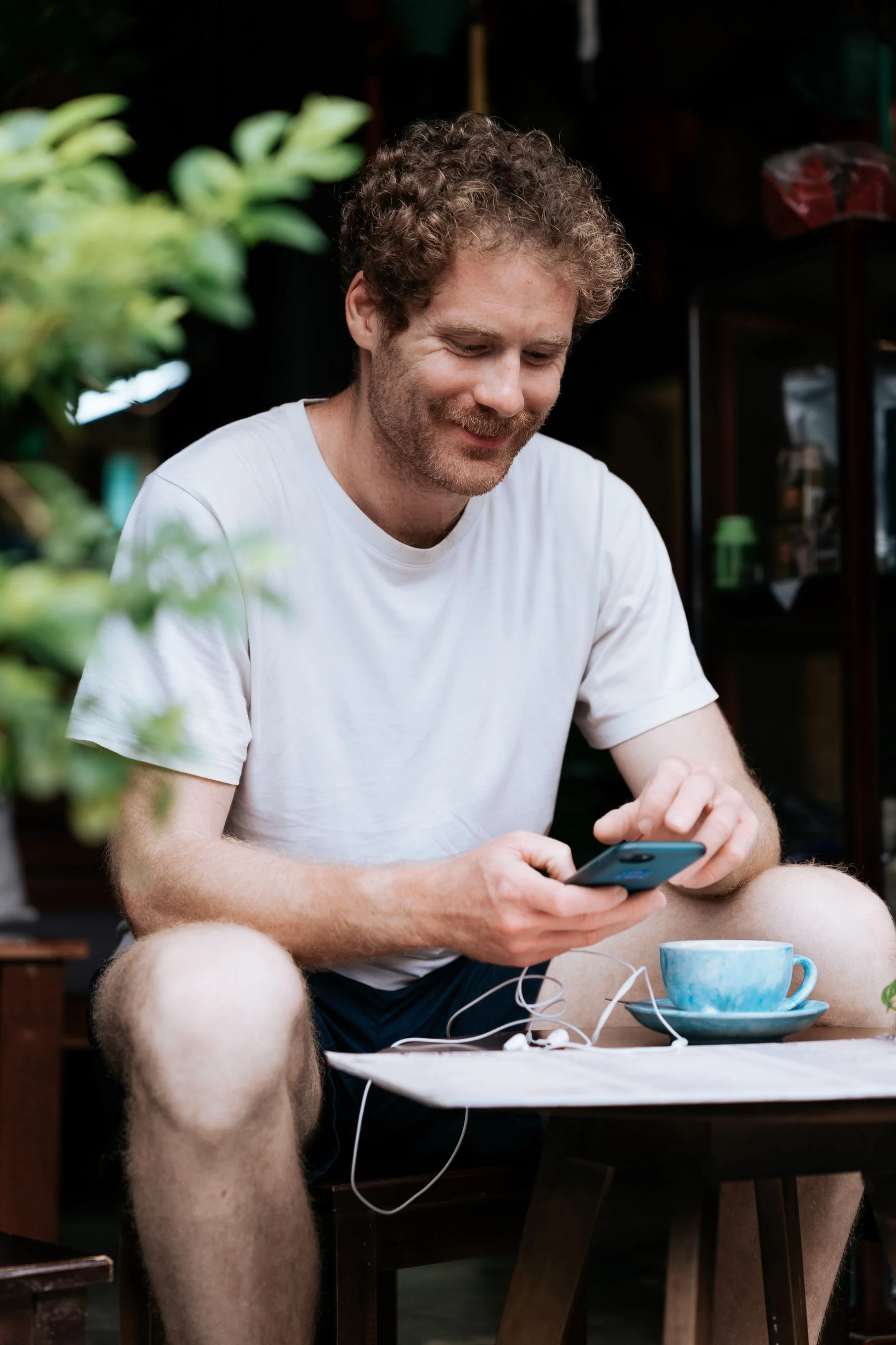 A casually dressed man smiling at his phone at an outdoor café